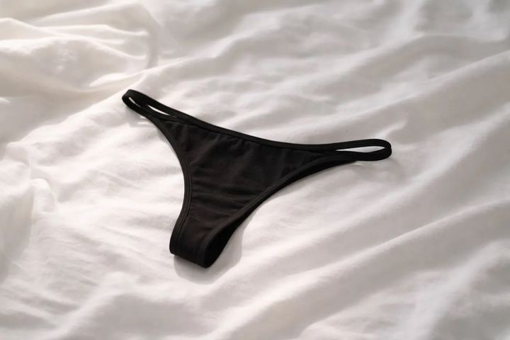 Black thong, worn, lying on a bed